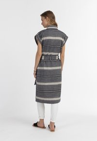 Completo in cotone stampato con maniche corte, vita con cintura, e design lungo fino al ginocchio in righe orizzontali blu navy e crema, abbinato a pantaloni bianchi.
