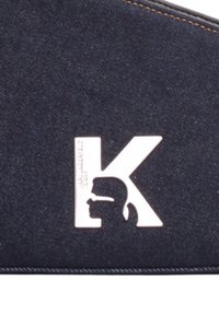 Surface en tissu bleu foncé avec un logo blanc "K" contenant une silhouette de profil portant des lunettes à l'intérieur de la lettre.