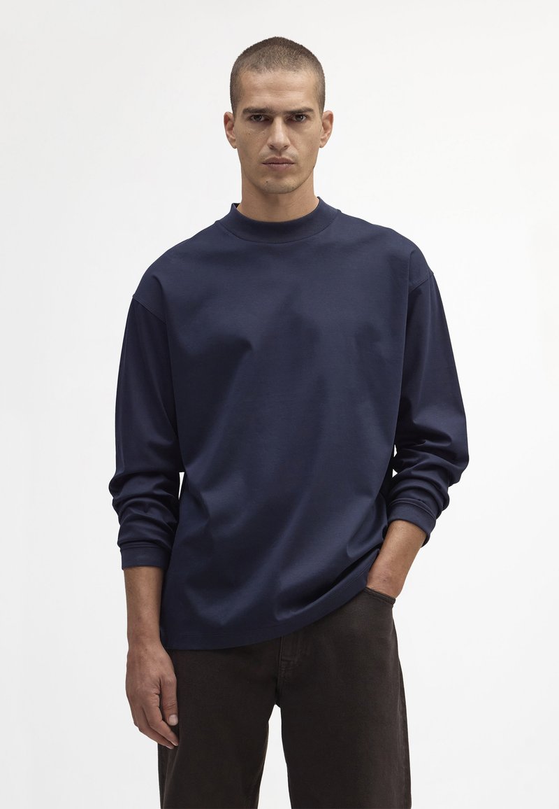 Navy niebieska koszulka z długim rękawem, z wysokim okrągłym dekoltem i luźnym krojem. Miękka, gładka tekstura, z opadającymi ramionami i minimalistycznym wzornictwem.