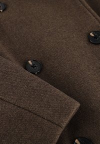 Brun uldfrakke med en blød tekstur. Har to sorte knapper, en dobbeltradet design og en moderne skræddersyet silhuet.