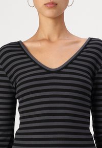 Dlouhý rukáv top s černými a tmavě šedými vodorovnými pruhy, hlubokým výstřihem do V a ribbovanou texturou.