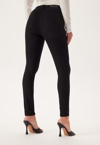 Jeans skinny neri realizzati in denim con una superficie liscia, dotati di due tasche posteriori e una vita alta, abbinati a mule nere con tacco.