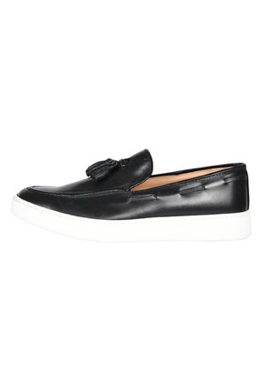 Scarpa slip-on in pelle nera con suola in gomma bianca, caratterizzata da cuciture decorative e un piccolo dettaglio con nappe sulla parte superiore.