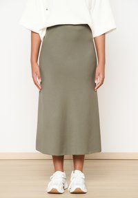 Olive green midi skirt made of textured fabric, featuring a high waist and a flowing silhouette, paired with white athletic shoes.