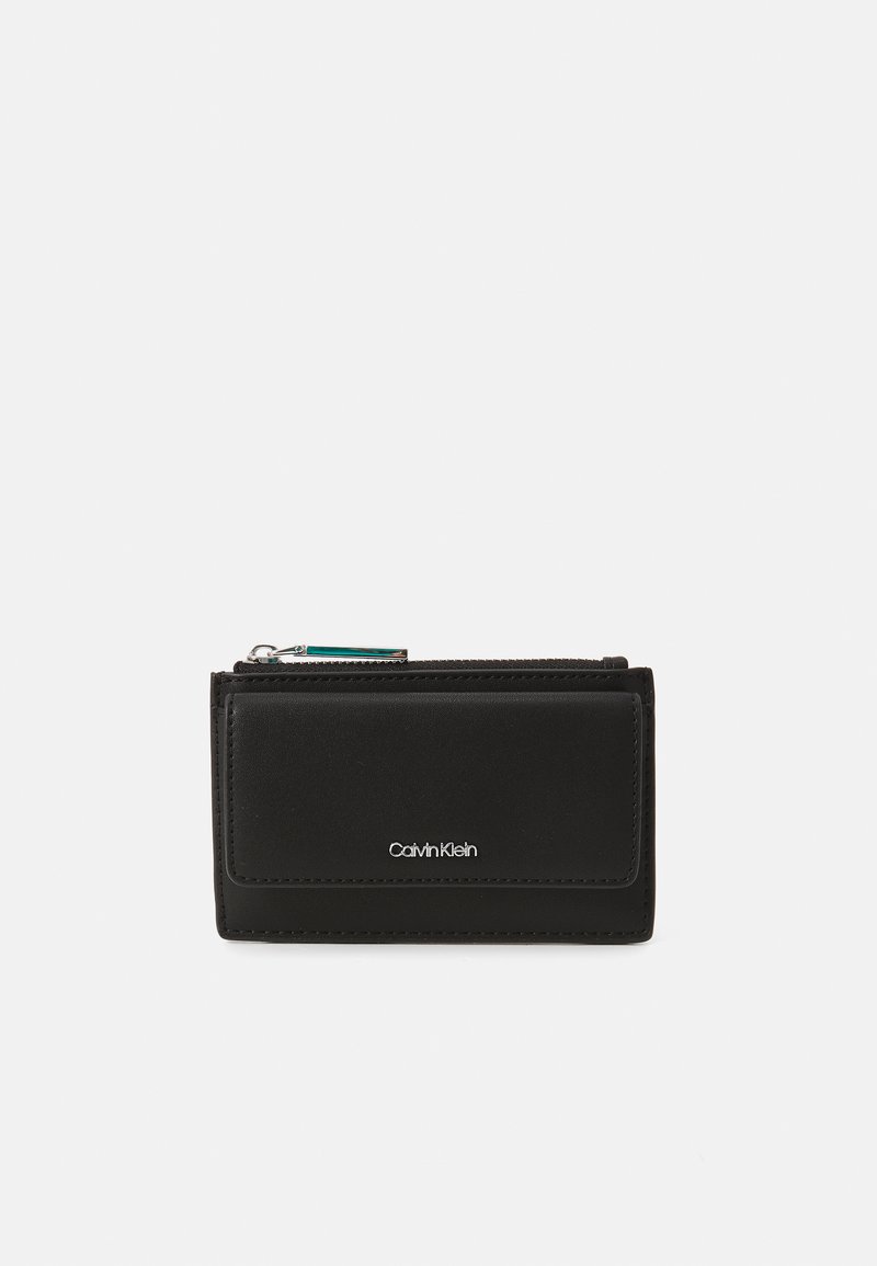 Portefeuille en cuir noir avec une texture lisse, doté d'une fermeture éclair et d'un petit logo argenté à l'avant. Forme rectangulaire compacte.