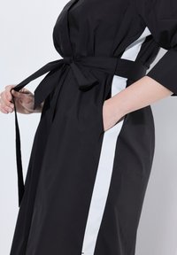 Abito nero avvolgente con cintura, con pannelli laterali bianchi. Realizzato in tessuto morbido, presenta un design elegante e tasche laterali.