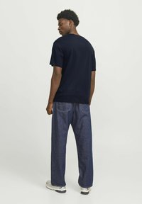 Marineblå bomulds t-shirt med rund halsudskæring, korte ærmer, parret med løstsiddende mørke denim jeans og hvide sneakers.