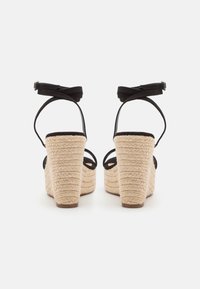 Mustad espadrillid, mille kontsad on kootud jute'ist, musta värvi, crisscross-sangaritega ja siledast materjalist jalaplaadi ning tekstuurse disainiga.