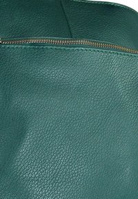 Sac à main en cuir texturé turquoise avec des coutures visibles et une fermeture éclair dorée sur la partie supérieure.