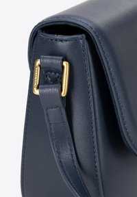 Marineblaue Leder-Schultertasche mit glatter Oberfläche, ausgestattet mit einer goldfarbenen Metallschnalle am verstellbaren Riemen und sichtbaren Nahtdetails.