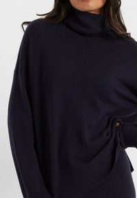 Navyblauwe coltrui van zacht breiwerk, met een ontspannen pasvorm, verlaagde schouders en ribgebreide manchetten met een subtiele naaddetail.