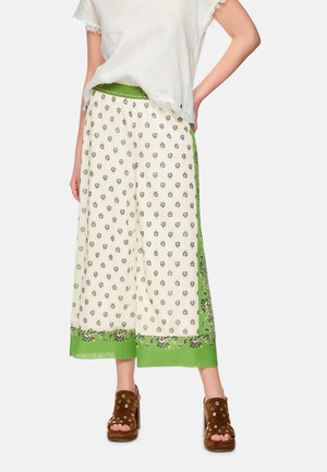 Woman wearing white cropped pants with small floral print and green borders, paired with brown heeled sandals and a white short-sleeve top.