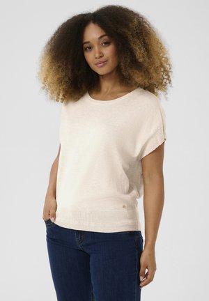 Pull en beige clair à coupe ample avec des manches courtes, ourlet inférieur côtelé et petite touche métallique. Associé à un jean bleu foncé.