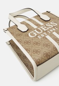 Sac fourre-tout marron à motifs avec des rayures blanches. Il présente un matériau texturé, deux anses supérieures et un logo embossé bien visible à l'avant.