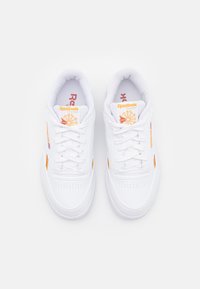 Ténis brancos de desporto com acentos laranja, bico perfurado, atacadores planos e colarinho acolchoado. Apresentam a marca na língua e na lateral.