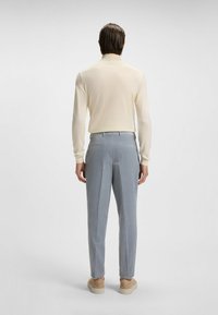 Lichtbeige longsleeve top gecombineerd met lichtgrijze broek met streepjes. De stof lijkt glad en op maat gemaakt. Zachte, casual schoenen maken de look compleet.