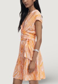Vestido envolvente naranja con mangas cortas, que presenta una cintura con lazo, un patrón abstracto blanco y una falda acampanada. Textura de tela suave.
