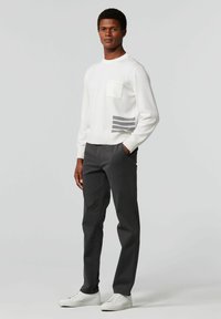 Witte gebreide trui met een borstzak en grijze streepdetails. Gemaakt met grijze broek en witte sneakers, wat een casual look creëert.