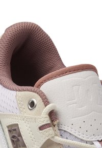 White sneaker with mesh and leather materials. Soft mauve collar, textured detailing, and silver eyelet. Features a prominent logo.