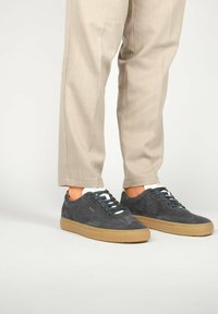 Zapatillas de ante gris con cordones planos, costuras tonales y una suela de goma. Usadas con pantalones ajustados beige claro.