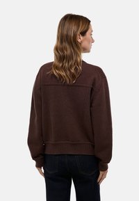 Pull en maille marron, à coupe décontractée, avec des poignets et une taille côtelés, présentant un design texturé à l'arrière et des épaules arrondies.