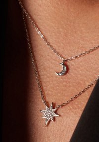 Zilveren gelaagde halskettingen met een sterpendant met heldere stenen en een sikkelmaanketting. De schakelkettingen zijn delicaat en dun.