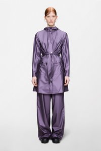 Μωβ αδιάβροχο παλτό με κουκούλα που σφίγγει με κορδόνι, μακριά μανίκια και ζώνη στη μέση. Συνδυασμένο με άνετο παντελόνι σε ίδιο χρώμα και μαύρα παπούτσια.