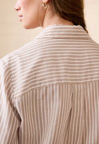 Chemise beige clair avec fines rayures blanches. Dotée d'un col classique et d'une texture lisse. Vue de dos, dévoilant les détails des coutures.