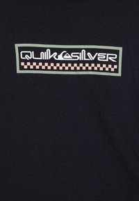 T-shirt nera in cotone con un design logo rettangolare che presenta "Quiksilver" in bianco in corsivo, accentuato da un bordo verde e un motivo a scacchi pesca.