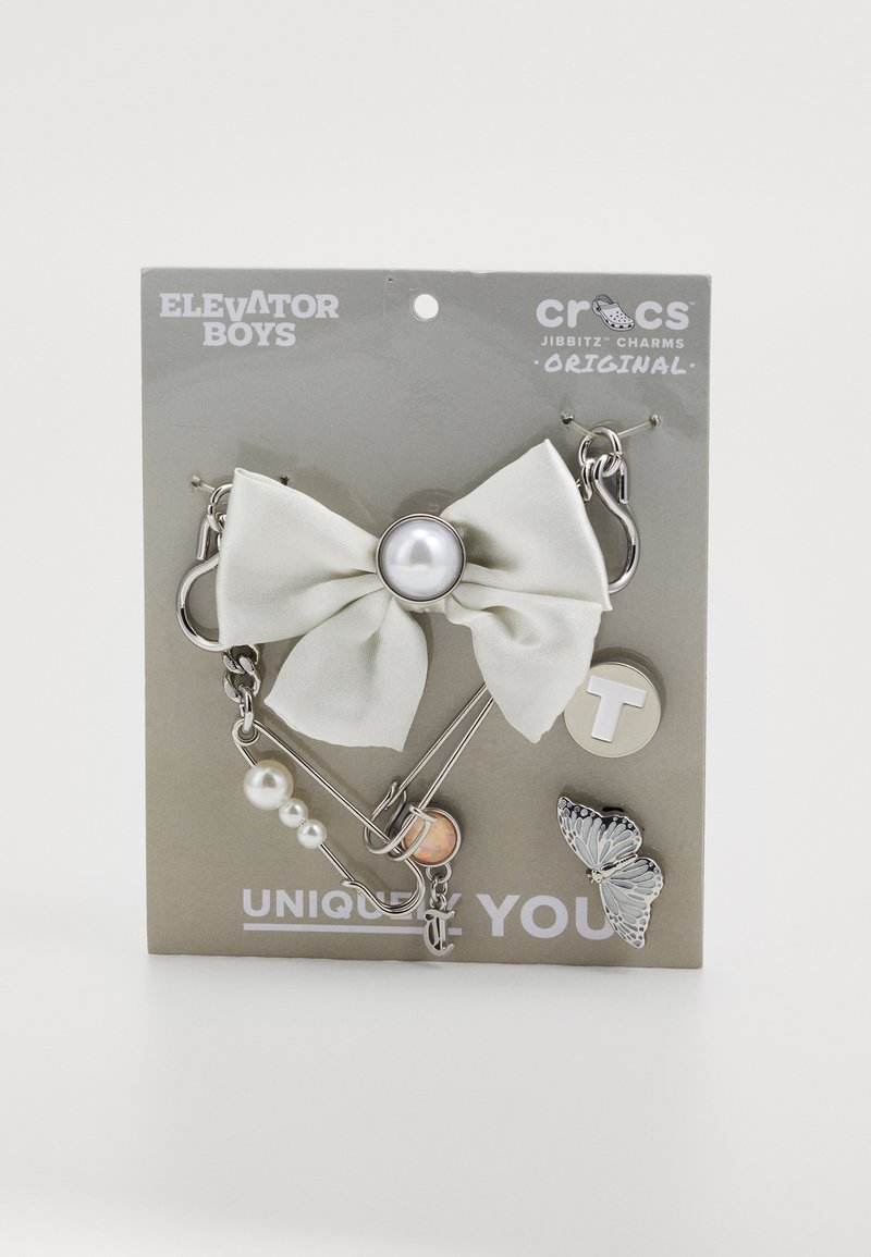 Crocs Jibbitz charms set featuring a large cream bow, silver hardware, pearl accents, a butterfly design, and a round letter "T" charm.