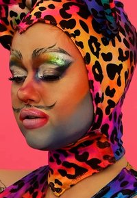 Fargerik leopardmønster hodehåndkle, dristig sminke med klare blå og korallfarger, intrikate detaljer på øynene og styliserte skjeggaccent.