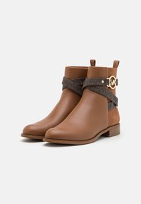 Bottines en cuir marron à fini lisse, dotées d'une sangle texturée foncée et d'un accent en métal doré. Talon bas empilé pour la stabilité.