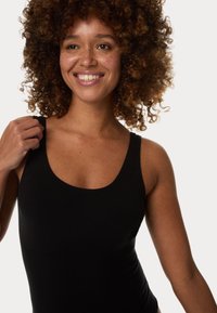 Top nero senza maniche con scollatura a forma di barco e spalline larghe. Il tessuto sembra elastico, creando una silhouette aderente. Sottile texture a coste.
