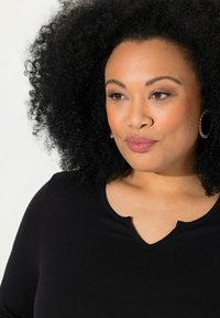 Haut noir à manches longues avec un décolleté en V subtil, texture lisse et design épuré. Porté avec des boucles d'oreilles circulaires.