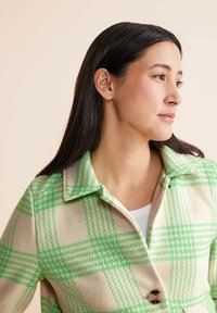 Giacca in lana a quadri verde e beige con ampio colletto, maniche lunghe e chiusura con bottoni. Presenta un tessuto testurizzato con motivo a scacchi.