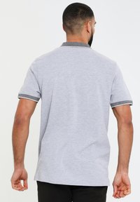 Grå kortærmet polo shirt med en struktureret sort krave, der har en regulær pasform og glat stof, set fra ryggen.