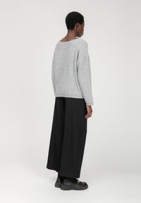 Maglione grigio con texture e vestibilità rilassata, abbinato a pantaloni larghi neri. Scarpe nere con suola spessa completano l'outfit.