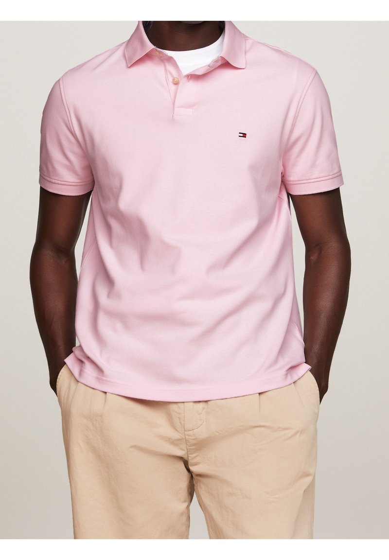 Polo rose clair en coton avec une coupe classique. Il présente une patte de boutonnage à deux boutons et un petit logo sur la poitrine gauche.