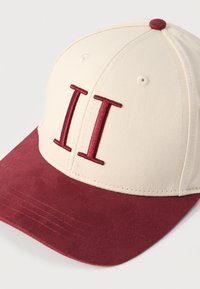 Μπεζ και μπορντό καπέλο бейζбол με κεντητό διπλό κάθετο σύμβολο στην μπροστινή επιφάνεια και μπορντό στέκα από σουέτ.