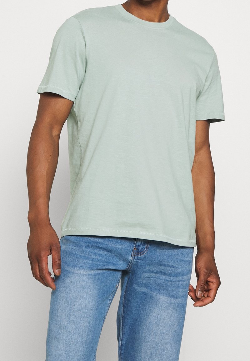 Lys grøn bomulds t-shirt med rund hals, korte ærmer og en afslappet pasform, parret med blå denim jeans. Minimale synlige stikninger.