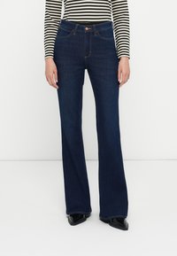 Dunkelblaue Schlagjeans aus Denim, mit fünf Taschen, sichtbaren Nähten und einem Knopfverschluss an der Taille. Strukturiertes Material.
