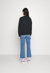 Sweatshirt en coton noir avec col rond, coupe décontractée et poignets côtelés, associé à un jean évasé bleu clair et des baskets multicolores.