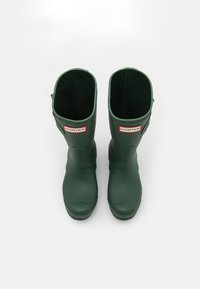 Botas de goma verdes hasta la rodilla con una textura suave, puntera redondeada y una destacada etiqueta 'HUNTER' en la parte delantera.