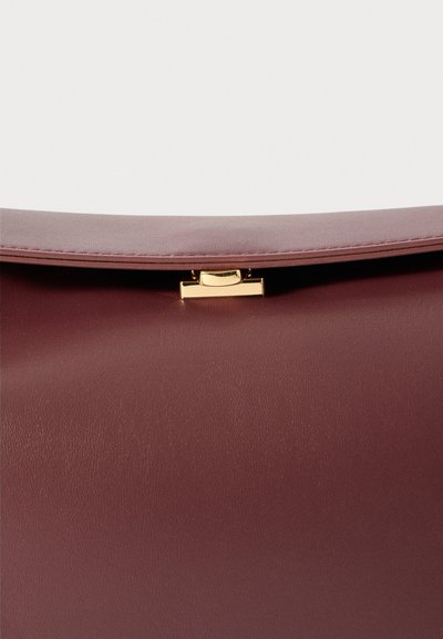 Detailní záběr na vínovou koženou tašku s klopou a zlatým obdélníkovým zámkem.