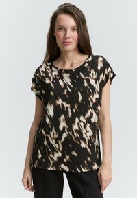 Krátký rukáv blouse v černé, hnědé a krémové abstraktní vzoru. Hladká tkanina s uvolněným střihem a kulatým výstřihem.