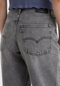 Šedé džíny z denimu s zadními kapsami s kontrastním prošíváním a černou značkovou etiketou na pase. Texturovaná tkanina s vybledlým vzhledem.