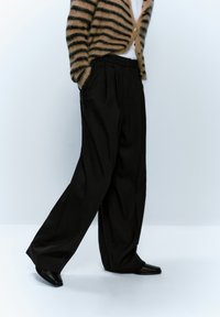 Pantalons larges noirs avec des plis, en tissu lisse. Associés à un cardigan rayé marron clair et noir, avec des boutons.