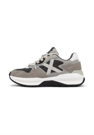Zapatilla deportiva gris y negra con materiales de ante y malla, que cuenta con un diseño distintivo en forma de X, suela de goma y acentos en blanco en el talón.