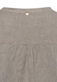 Leinenbluse in hellbeige mit einem gefalteten Rückendetail und einem runden Ausschnitt. Verfügt über ein kreisförmiges Metall-Logo-Accessoire am Hals.