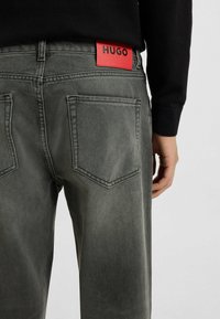 Grijze denim jeans met een vervaagde afwerking, vijf-pocket ontwerp en een rood "HUGO" label op de tailleband. Textuurstof en gestructureerde vorm.